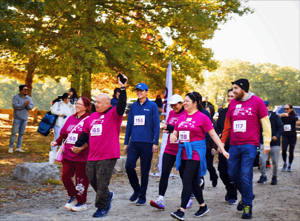 A group of walkers wearing bright magenta shirts and race bibs participate in the Family Fun Run & Walk event.