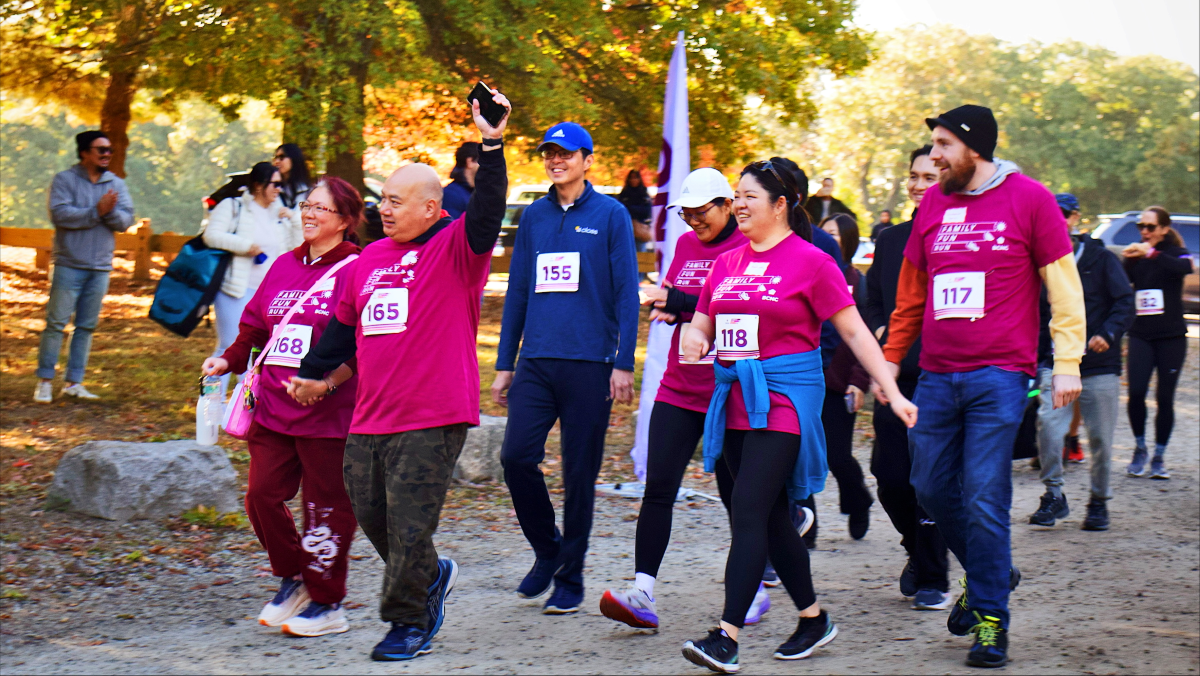 A group of walkers wearing bright magenta shirts and race bibs participate in the Family Fun Run & Walk event.