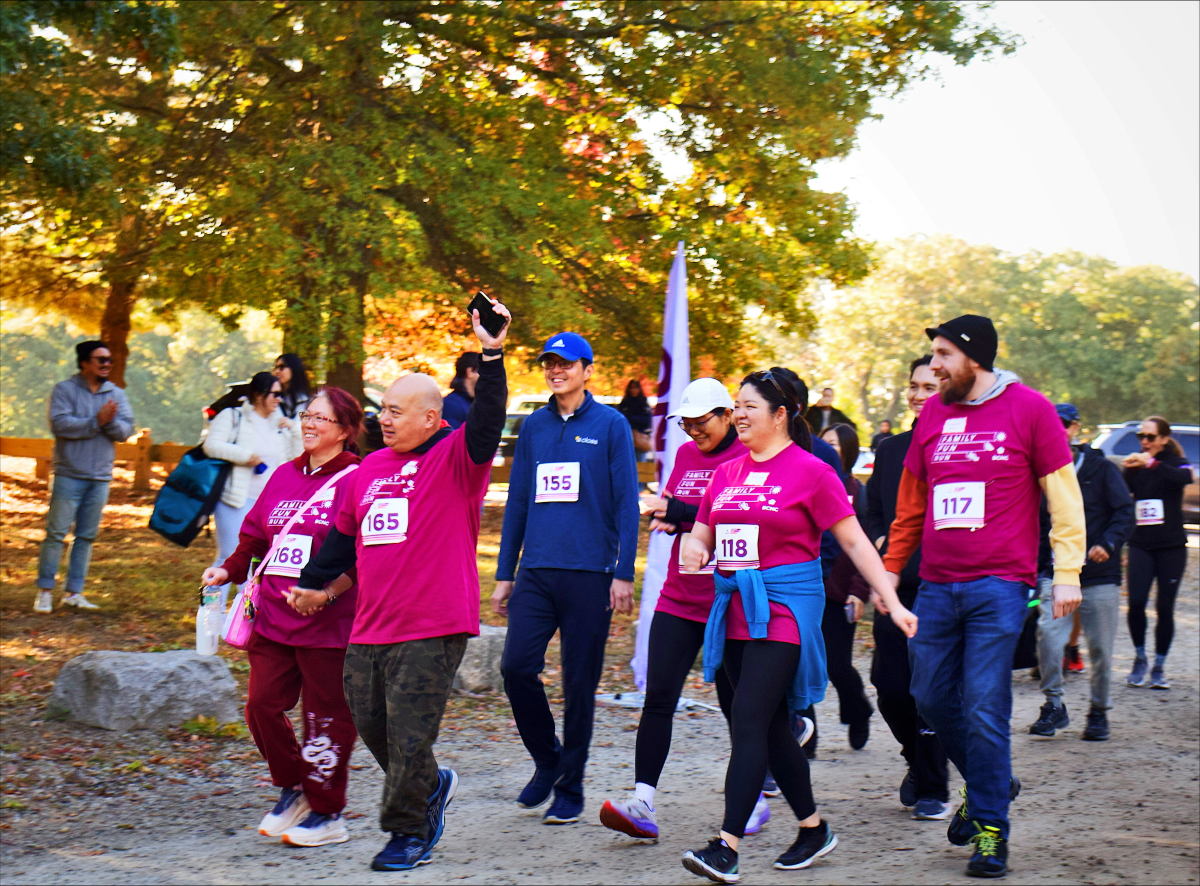 A group of walkers wearing bright magenta shirts and race bibs participate in the Family Fun Run & Walk event.